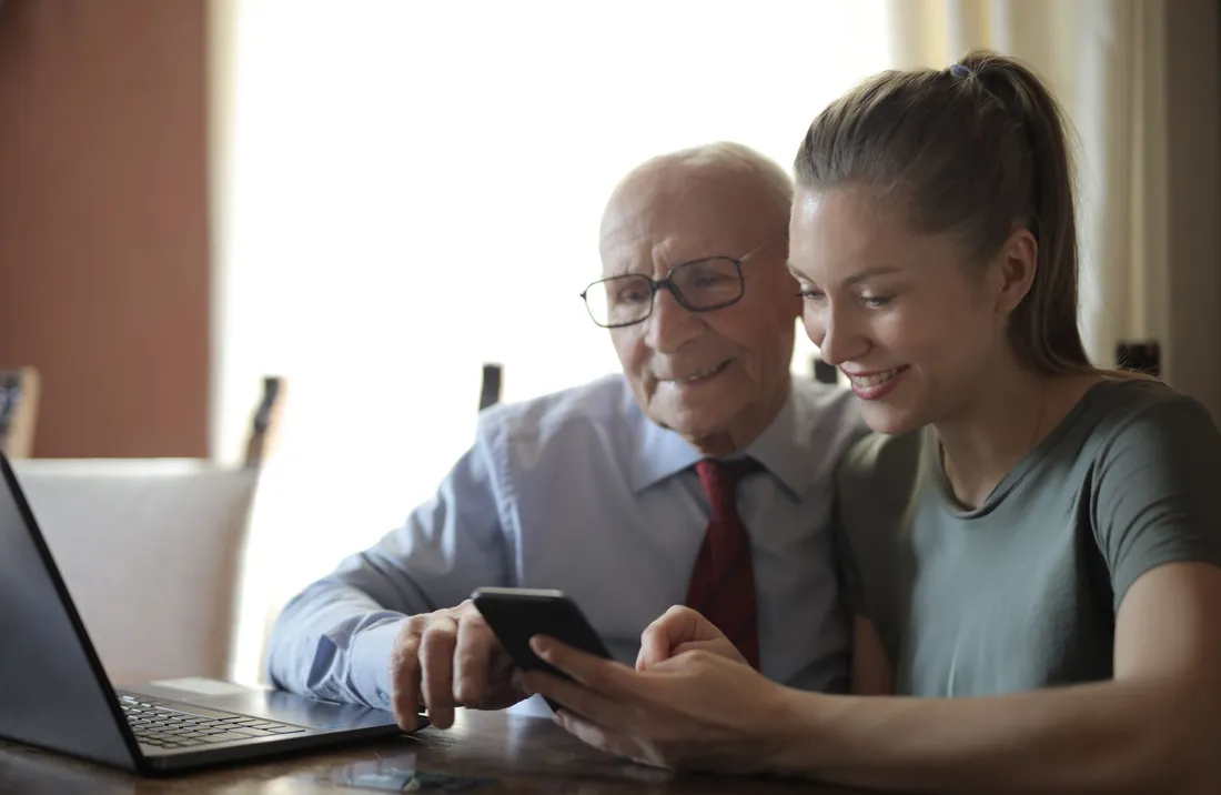 Eine junge Frau schaut mit ihrem Großvater lachend aufs Handy